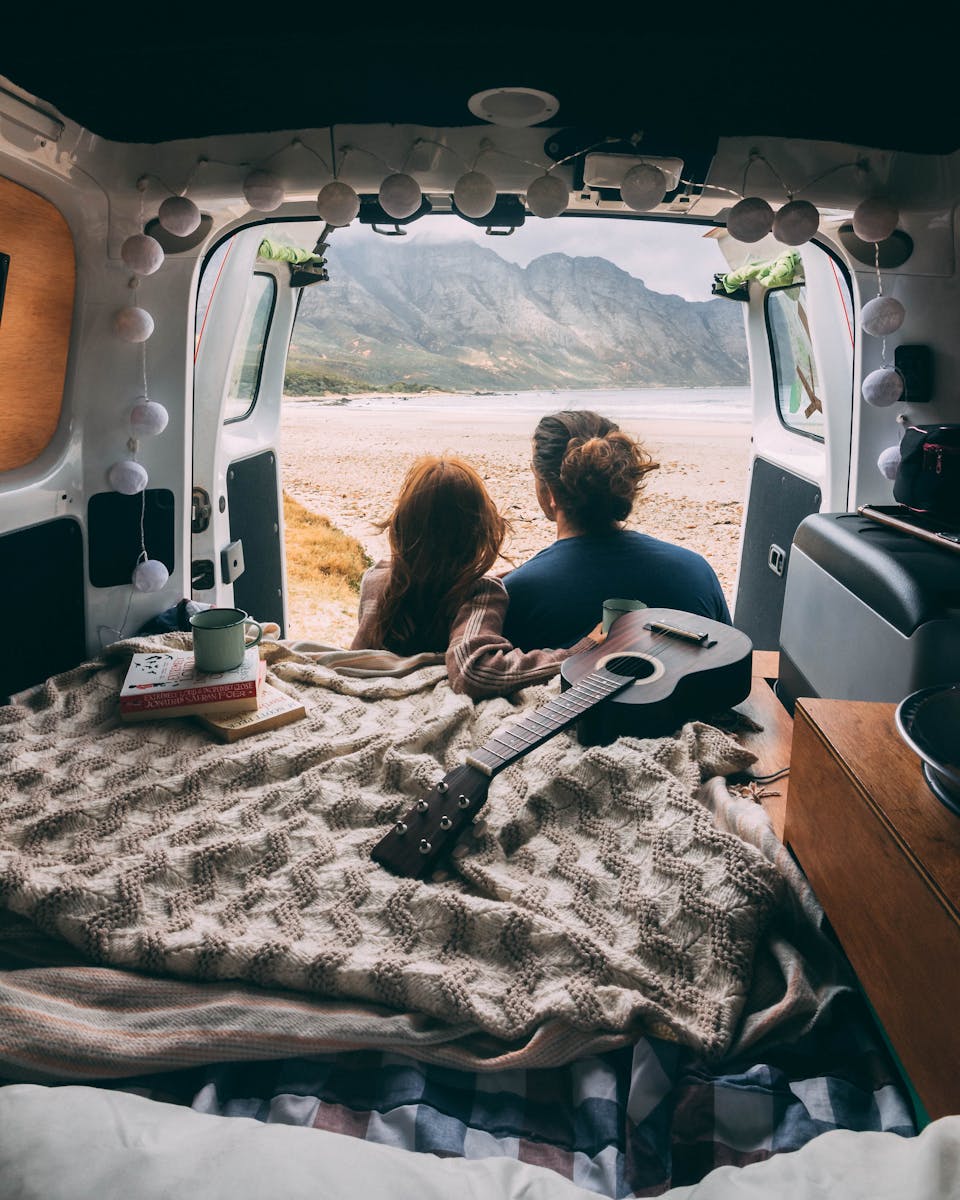 Back view of a couple sitting on a camper van, looking at a scenery
