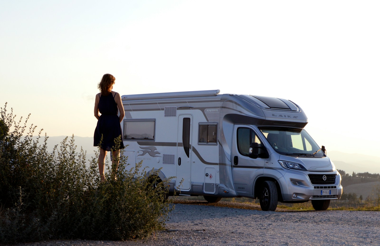 woman in black dress standing beside white and blue rv trailer during daytime, RV